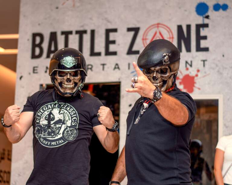 Two players in skull masks at the Battle Zone logo wall