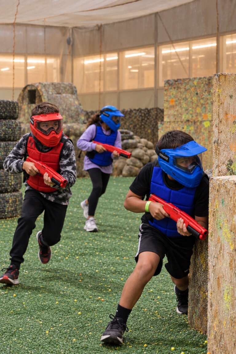 Juniors in masks and padded vests with kids’ paintball markers moving through the Battle Zone arena